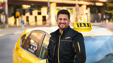 Freundlicher Taxilenker steht vor dem Taxi